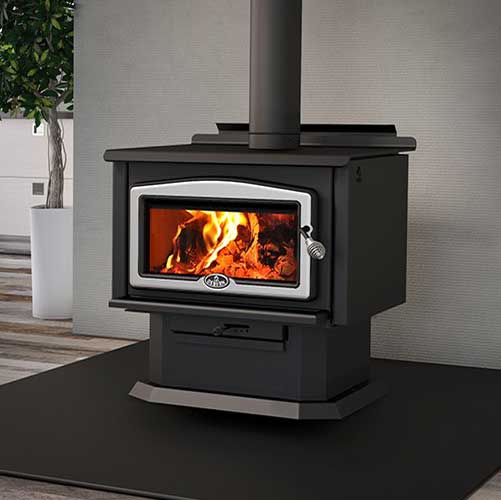 Osburn 2400 Wood Stove black base with silver around the glass on the door and gray wall background.  Tree to the left.