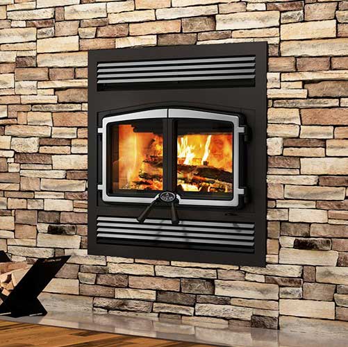 Large fireplace with double door and brushed steel frame.  The surrounding of the fireplace is black Stratford-Large-Wood-Fireplace.  There is a stacked stone wall in the background.