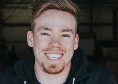 Jonah Lindley - Blondish hair long on top and shaved on sides. Brown eyebrows, blue eyes and reddish mustache and goatee. Beautiful smile with white straight teeth wearing Ashbusters jacket.