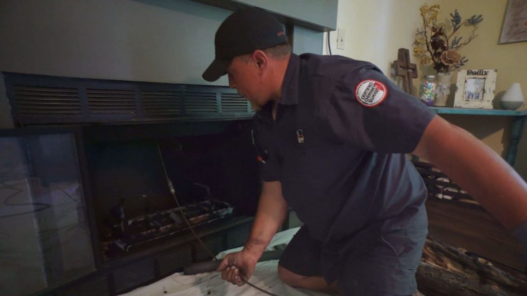 chimney sweep wearing black shirt and hat cleaning a chimney
