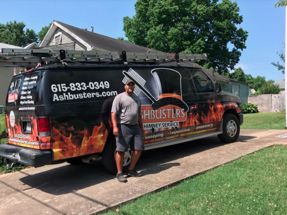Tech standing in front of work truck that says Ashbsuters Chimney Service in front of home with concrete drive