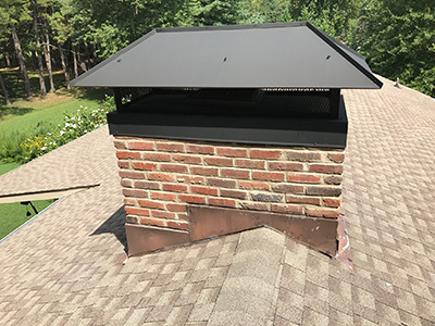 brown bricked chimney with new black metal chimney cap on roof