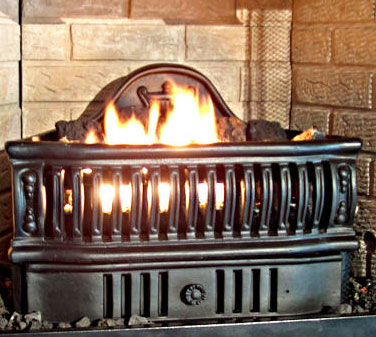 Black fireplace with open venting across front tan bricks behind it and a firing burning in it