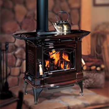 Stock Photo- Hampton H300 Large Wood Stove -Ashbusters Chimney - Nashville TN large black wood stove with four legs and kettle on top of it a fire burning in it and bricks on the wall behind