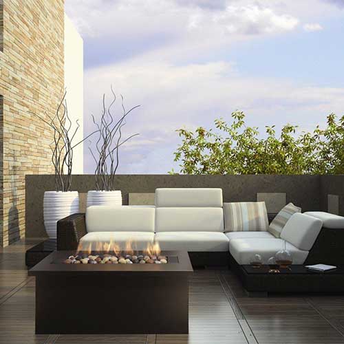 Outdoor gas fireplace with corner sofa and plants with blue sky.