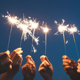 6 hands holding sparklers over a dark blue sky